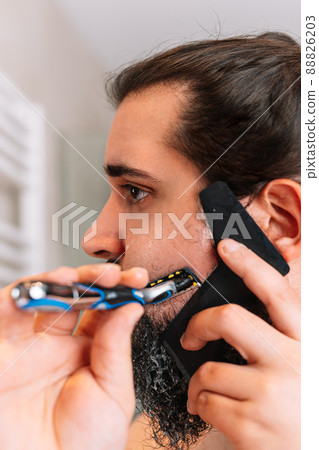 young man with a long beard, shaving with a safety razor 88826203