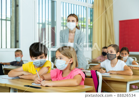 Preteen pupils in protective masks studying in classroom with female teacher 88826534