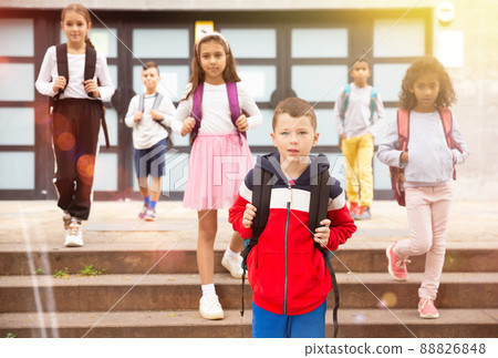 Positive boy standing near school, children on background Positive boy standing near school, children on background 88826848