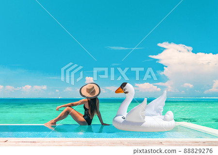 Luxury swimming pool vacation travel lady sun tanning relaxing on infinity ocean waterfront resort with floating white swan inflatable toy float banner panoramic summer background 88829276