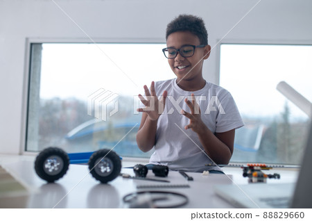 A cute teen sitting at the table and playing with toy wheels 88829660
