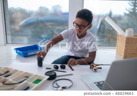 A cute teen sitting at the table and playing with toy wheels A cute teen sitting at the table and playing with toy wheels 88829661