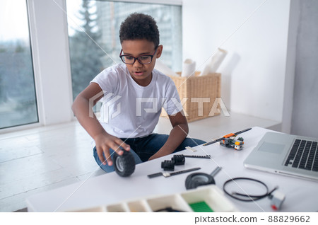 A cute teen sitting at the table and playing with toy wheels A cute teen sitting at the table and playing with toy wheels 88829662