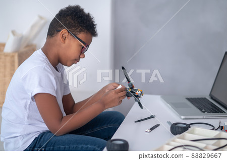 A dark-skinned boy constructing a transformer and looking busy A dark-skinned boy constructing a transformer and looking busy 88829667