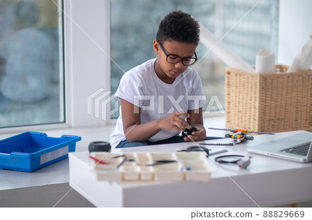 A dark-skinned boy constructing a transformer and looking busy A dark-skinned boy constructing a transformer and looking busy 88829669