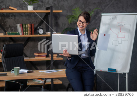 Smiling woman with laptop in hands smiling and waving her hand 88829706