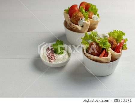 Two servings of mini pita with falafel .vegetables and sauce. On a light wooden background. Street food Two servings of mini pita with falafel .vegetables and sauce. On a light wooden background. Street food 88833171