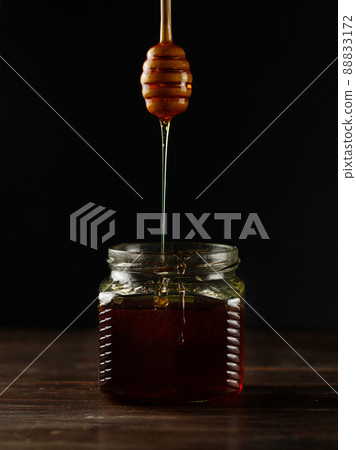 Dark honey drips from a wooden spoon into a jar. Close-up, low key. Dark honey drips from a wooden spoon into a jar. Close-up, low key. 88833172