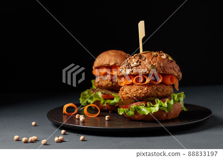 Two vegetarian burgers with chickpea cutlet or chechivitsa with fresh vegetables and pickled cucumbers. On a black background, low key 88833197