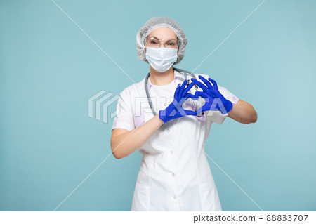 Heart symbol, love. Doctor or nurse woman in a personal protective suit with a stethoscope, on a blue background. In a mask, gloves, goggles and a hat. Copy paste. healthcare concept. Heart symbol, love. Doctor or nurse woman in a personal protective suit with a stethoscope, on a blue background. In a mask, gloves, goggles and a hat. Copy paste. healthcare concept. 88833707