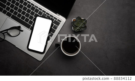Stylish workplace with smart phone, laptop computer and coffee cup on dark stone background. Top view. 88834112