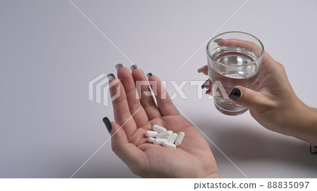 Woman holding pills and a glass of water in hand. Healthcare, medicine, treatment, therapy concept. Woman holding pills and a glass of water in hand. Healthcare, medicine, treatment, therapy concept. 88835097