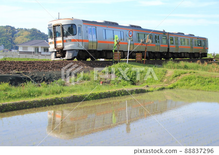 A diesel car passing through an unmanned railroad crossing on the embankment next to a paddy field filled with water A diesel car passing through an unmanned railroad crossing on the embankment next to a paddy field filled with water 88837296