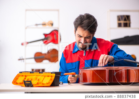 Young male repairman repairing musical instruments at workplace Young male repairman repairing musical instruments at workplace 88837438