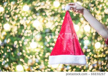 Shot of someone hand pinching Santa Claus hat with beautiful decorative Christmas light bokeh background. Symbol of Christmas festival and New Year is coming. Shot of someone hand pinching Santa Claus hat with beautiful decorative Christmas light bokeh background. Symbol of Christmas festival and New Year is coming. 88838267