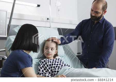 Careful parents talking with sick daughter about recovery period. Young mother and father discussing with ill child patient about consultation results and disease treatment while in recovery ward. Careful parents talking with sick daughter about recovery period. Young mother and father discussing with ill child patient about consultation results and disease treatment while in recovery ward. 88841214