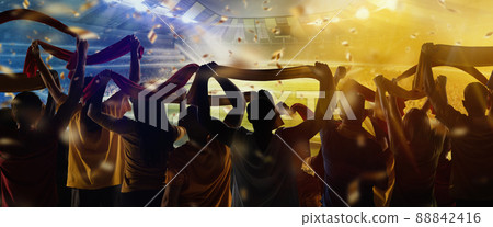 Victory. Back view of football, soccer fans cheering their team with state flags and scarfs at crowded stadium at evening time. Concept of sport, competition. Out of focus effect Victory. Back view of football, soccer fans cheering their team with state flags and scarfs at crowded stadium at evening time. Concept of sport, competition. Out of focus effect 88842416