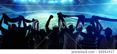 Back view of football, soccer fans cheering their team with state flags and scarfs at crowded stadium at evening time. Concept of sport, support, competition. Out of focus effect 88842417