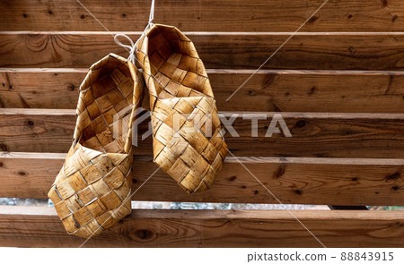 Birchen woven bast shoes hang on a log wall. Birchen woven bast shoes hang on a log wall. 88843915