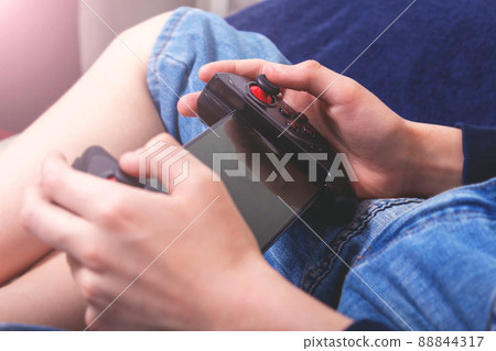 Teenager playing on his phone with console. Teenager playing on his phone with console. 88844317