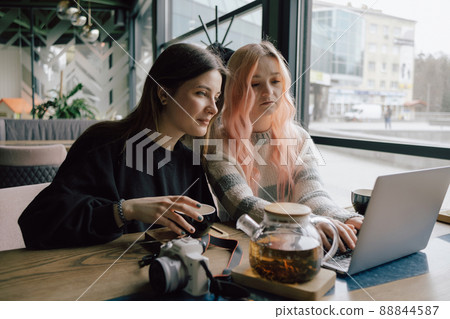 two happy young women sitting in coffee shop looking at laptop computer 88844587