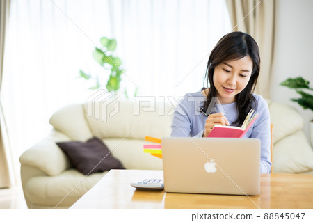 A woman in her thirties looking at a computer screen while taking notes while working from home 88845047
