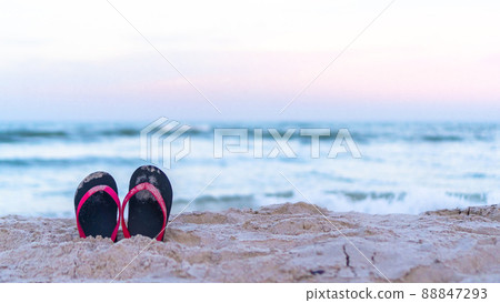 Sandy beach summer holiday vacation background with a pair of flip-flop sandals on hot sunny day on sea or ocean sand background with evening sky 88847293