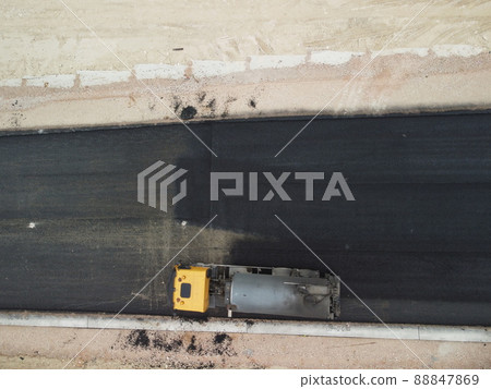 yellow truck pouring bitumen over a new road. Aerial drone shot. Road construction in progress on slope nature canyon. Infrastructure development and logistics. yellow truck pouring bitumen over a new road. Aerial drone shot. Road construction in progress on slope nature canyon. Infrastructure development and logistics. 88847869