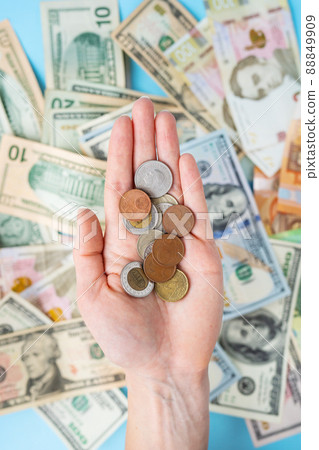 The girl holds coins in her hands against the background of scattered banknotes. International banknotes - dollars, euros, coins. The concept of currency transactions, loans, exchange, gambling. 88849909