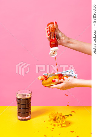 Food pop art photography. Female hands tasting hotdog with dark beer isolated on bright pink and yellow background. Vintage, retro style interior 88850310
