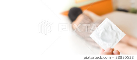 Human hand holding a packed condom against a blurred female background in white bed,copy space Human hand holding a packed condom against a blurred female background in white bed,copy space 88850538