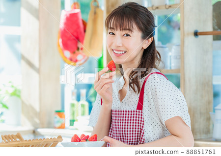 A woman picking and eating strawberries in the kitchen A woman picking and eating strawberries in the kitchen 88851761