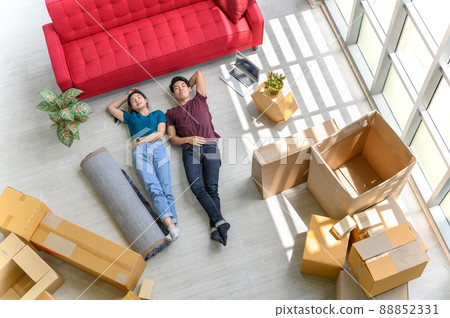 Top view of young asian couple smiling, relaxing and resting after unpacking cardboard boxes in new house with cardboard boxes on floor 88852331