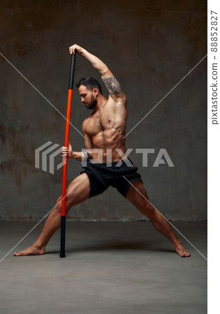 A ninja man holds on to a fighting stick and attacks close-up on gray studio background 88852827