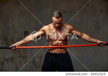 A fighter shirtless in black shorts, stands in a fighting artificially pose and holds a fight stick on studio background. A fighter shirtless in black shorts, stands in a fighting artificially pose and holds a fight stick on studio background. 88852829