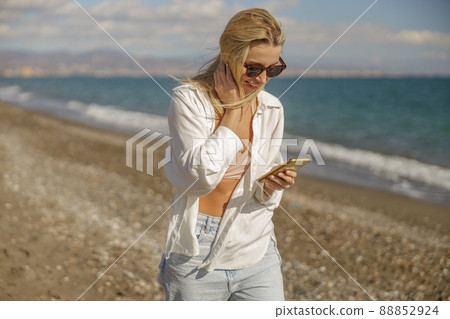 Content woman receiving message, using smartphone while strolling along the beach 88852924