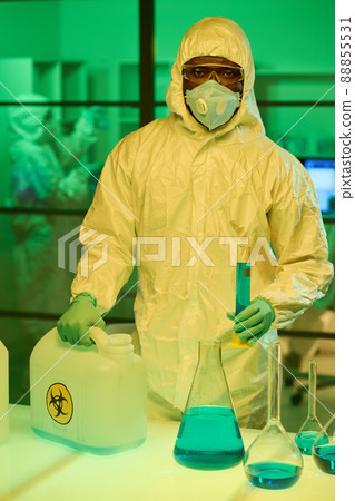 Modern scientist in coveralls holding canister and flask with liquid substance 88855531