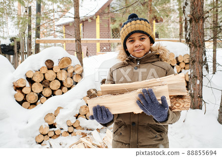 Cute little boy in warm winter jacket and knitted beanie holding firewood Cute little boy in warm winter jacket and knitted beanie holding firewood 88855694