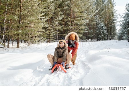 Cheerful African American man in winterwear pushing sledge with his son Cheerful African American man in winterwear pushing sledge with his son 88855767