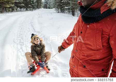 Happy cute little boy in winterwear looking at his father pulling sledge Happy cute little boy in winterwear looking at his father pulling sledge 88855768