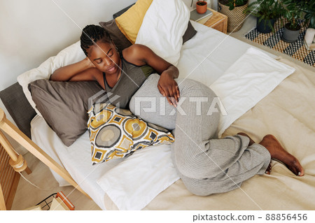 High angle view of African young girl looking at her pregnant belly while relaxing on cushions in bed High angle view of African young girl looking at her pregnant belly while relaxing on cushions in bed 88856456