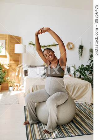 African young woman doing exercises on fitness ball in her bedroom during pregnancy African young woman doing exercises on fitness ball in her bedroom during pregnancy 88856478