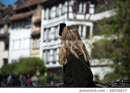 Portait on back view of woman taking a picture with phone at little France quarter in Strasbourg Portait on back view of woman taking a picture with phone at little France quarter in Strasbourg 88856637