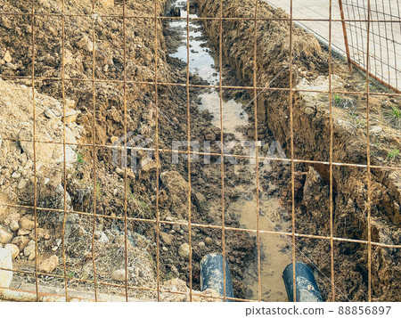 sandy ditch with communications. the moat is protected by a metal mesh in a new microdistrict of the city, pipes are being laid to bring communications to residential buildings 88856897