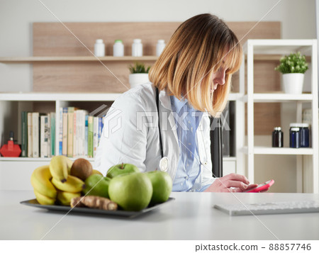 distracted female nutritionist chatting with smartphone in office studio 88857746