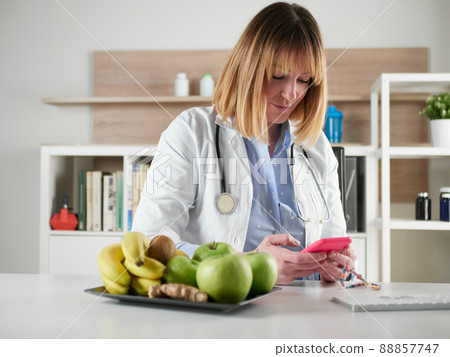 distracted female nutritionist chatting with smartphone in office studio 88857747