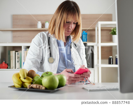 distracted female nutritionist chatting with smartphone in office studio 88857748