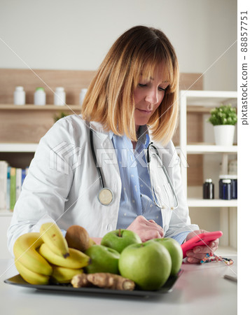 distracted female nutritionist chatting with smartphone in office studio 88857751