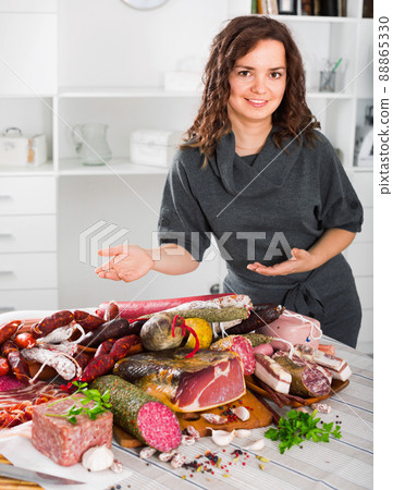 Woman costs near table on which sausages and smoked meat 88865330