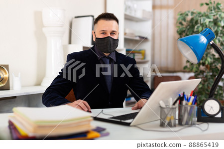 Man office manager wearing face mask while sitting in his workplace. Man office manager wearing face mask while sitting in his workplace. 88865419